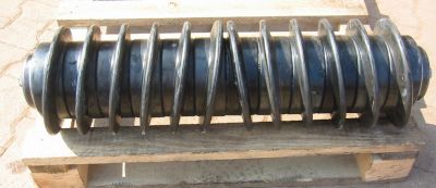 Heavy-duty spiral roller stored on a wooden pallet, designed to eliminate material build-up and improve belt tracking on conveyor belts