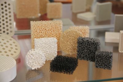 Presentation of various ceramic foam filters and extrusion filter shapes on a glass shelf, displaying different PPI sizes for foundry use